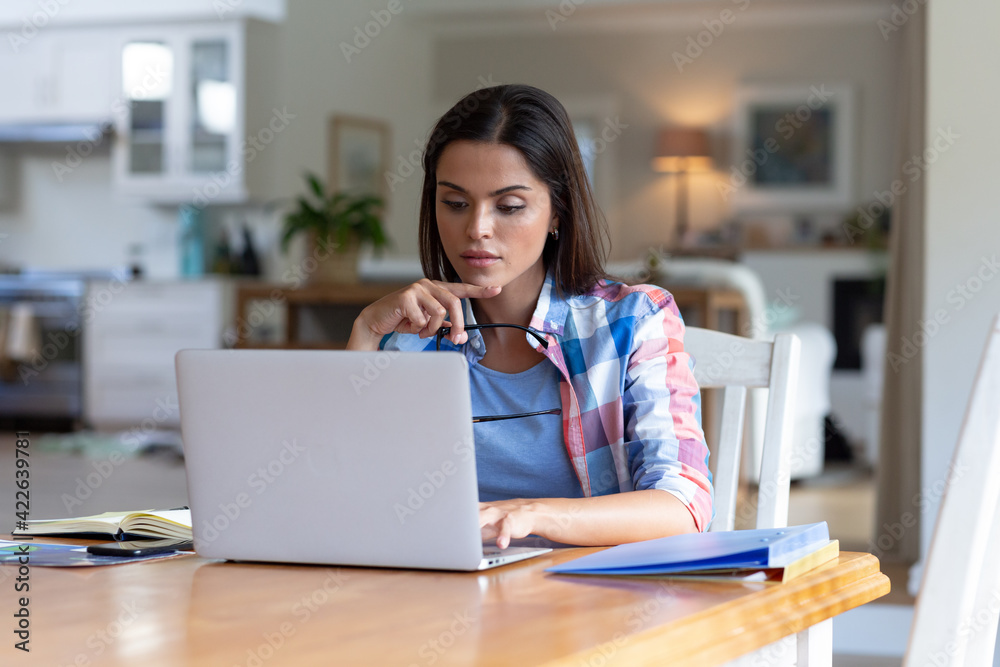 Caucasian woman sitting by desk working from home using laptop Caucasian woman sitting by desk working from home using laptop