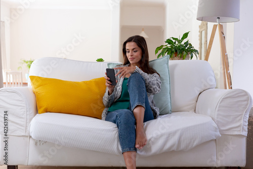 Caucasian woman sitting on a couch using smartphone and smiling
