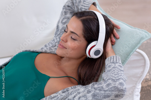 Caucasian woman lying on a couch listening to music on headphones and smiling
