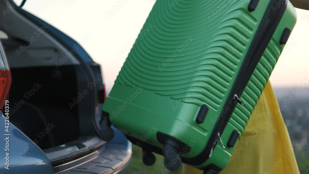 Young woman taking green suitcase from car trunk. Travel and vacations concept. Young woman taking green suitcase from car trunk. Travel and vacations concept.