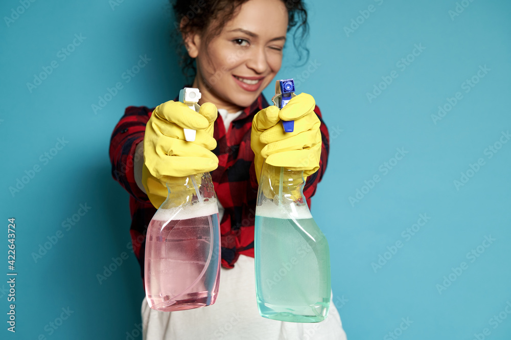 Beautiful young woman, housewife directs cleaning sprays as if shooting from a pistol, smiling maliciously and covering one eye at the camera. Focus on hands Beautiful young woman, housewife directs cleaning sprays as if shooting from a pistol, smiling maliciously and covering one eye at the camera. Focus on hands