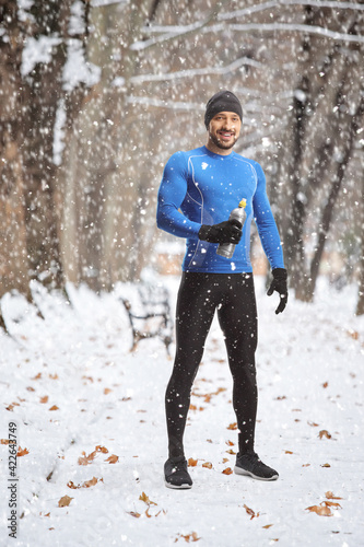 Fit man in running clothes holding a drink bottle on a snowy day outdoors © Ljupco Smokovski