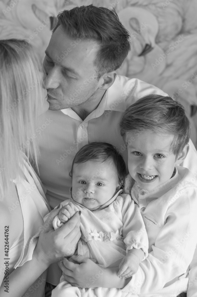 A happy family. Father, mother, son and baby daughter. The father holds the children in his arms and kisses his wife. Blacl and White. Exemplary family.