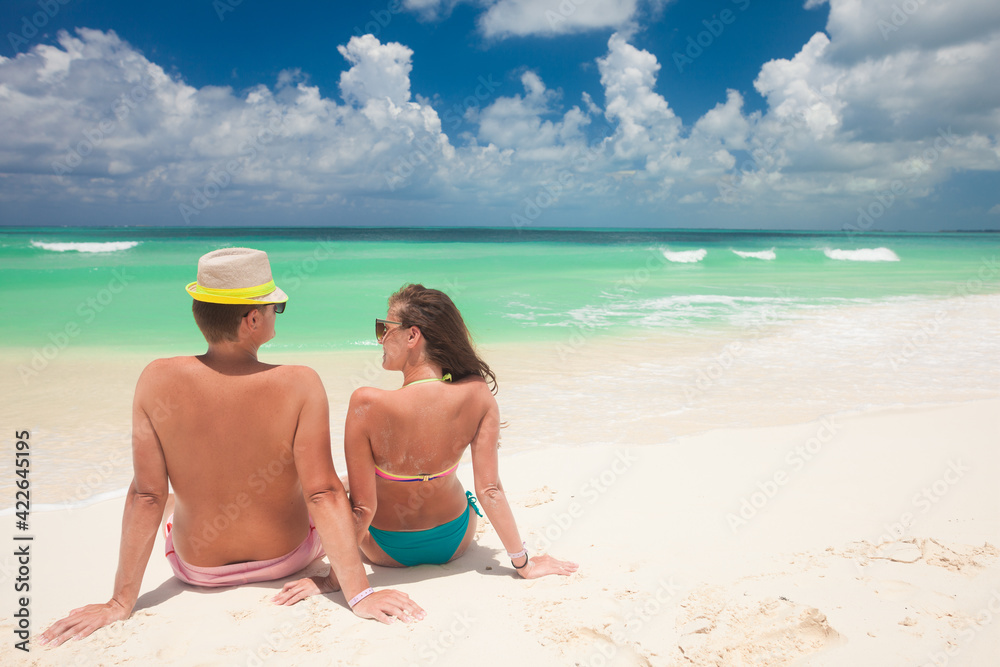 Back view of a man and woman couple sitting on caribbean white sand beach Back view of a man and woman couple sitting on caribbean white sand beach