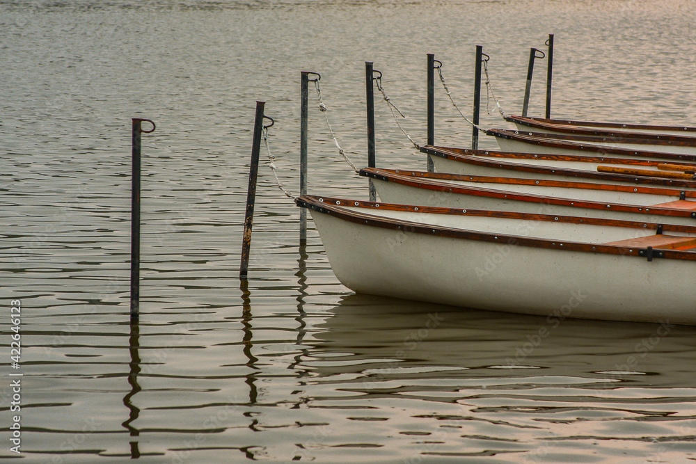 Small boats moored on masts on a lake. Wooden boats ready waiting in line on a calm water Small boats moored on masts on a lake. Wooden boats ready waiting in line on a calm water