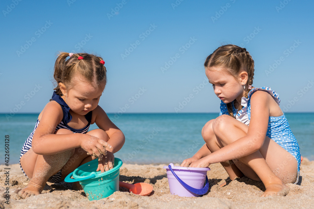 Children girls playing with sand at the beach in summer day. Kids building sand sculptures with shovels and buckets on coast sea. Fun family vacation concept Children girls playing with sand at the beach in summer day. Kids building sand sculptures with shovels and buckets on coast sea. Fun family vacation concept