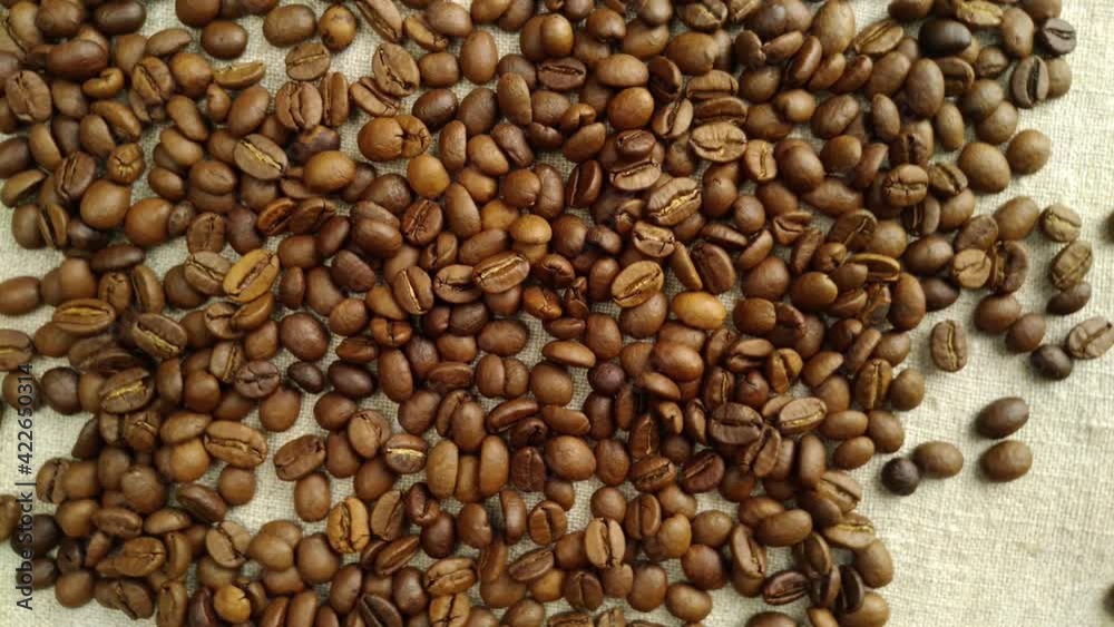 Aromatic coffee beans are randomly scattered on a textile napkin, in a slow rotation Aromatic coffee beans are randomly scattered on a textile napkin, in a slow rotation
