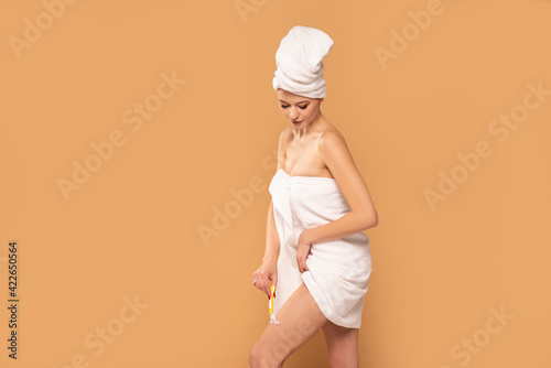 Beautiful girl in white towel on head shaving her legs. photo