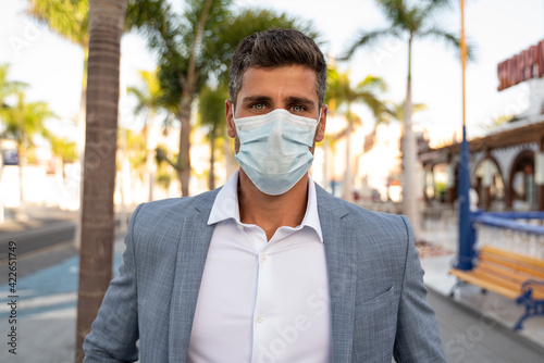 Handsome businessman with face mask for protection outdoors, looking at camera.