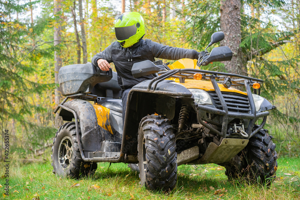 Fototapeta premium Man on a quad bike in forest. He drive through forest on ATV. Man on a yellow ATV. Concept - engaging in extreme sports. Quad bike driver posing on background of forest. Off-road driving on ATV