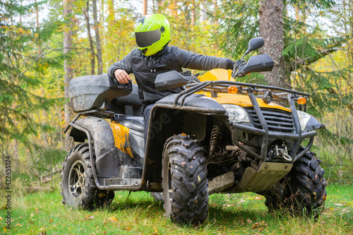 Man on a quad bike in forest. He drive through forest on ATV. Man on a yellow ATV. Concept - engaging in extreme sports. Quad bike driver posing on background of forest. Off-road driving on ATV