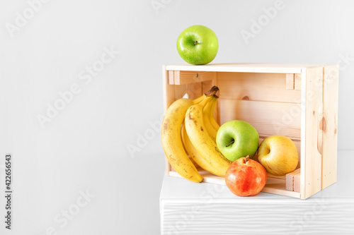 Fototapeta Naklejka Na Ścianę i Meble -  Organic fruits in wooden box against white wall. Donation box, fruit delivery or online shopping service. Text space. Social donating.