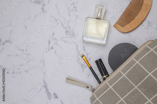 Gray makeup bag with cosmetic beauty products spilling out on to a marble table