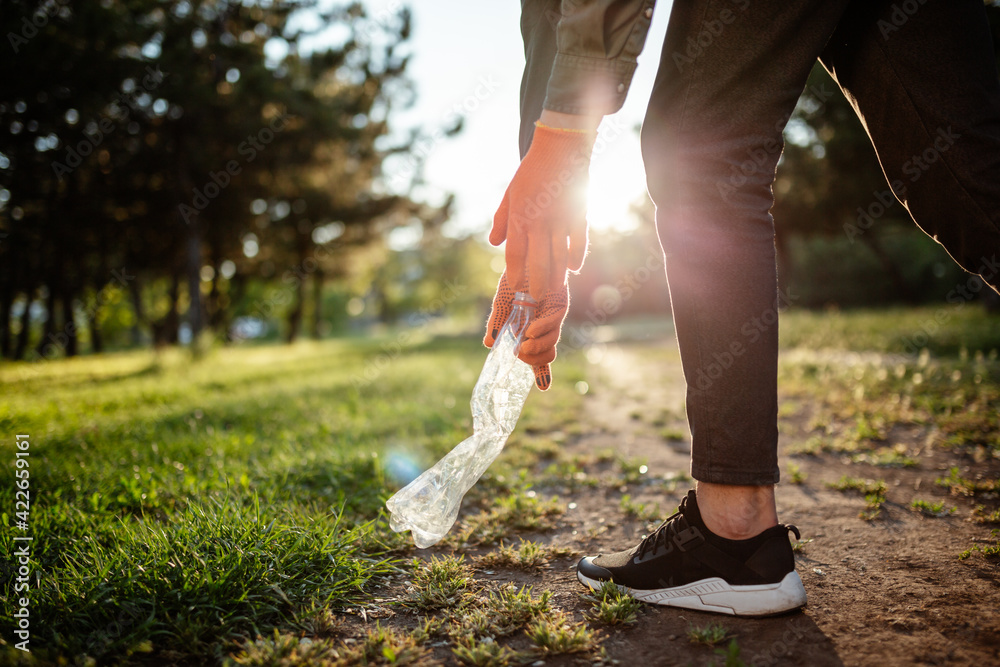 Man picks up litter outdoors, collecting used plastic bottle trash. A volunteer cleans up the park on a sunny bright day. Clearing, pollution, ecology and plastic concept.