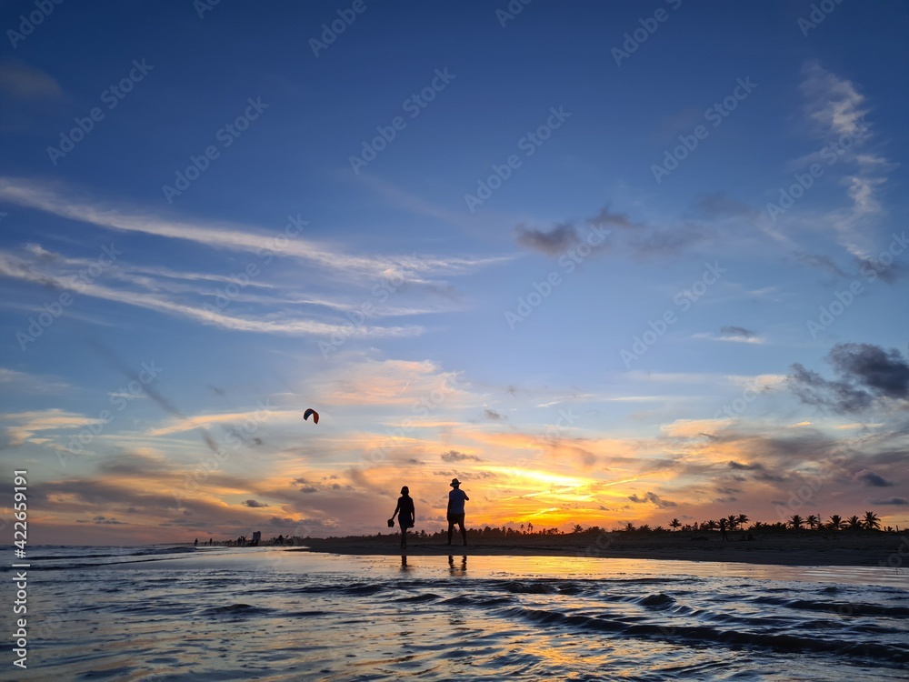 Silhuetas de pessoas e reflexos na água em um por do sol na praia