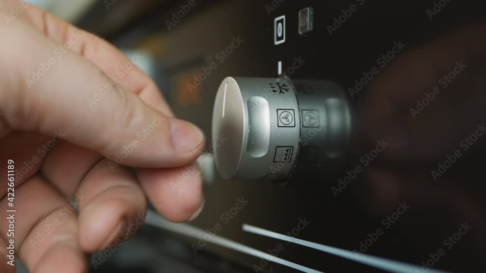Rotary knob on the stove. a man's hand extinguishes and turns on the temperature on the oven button. the hand turns the handle of the electric stove