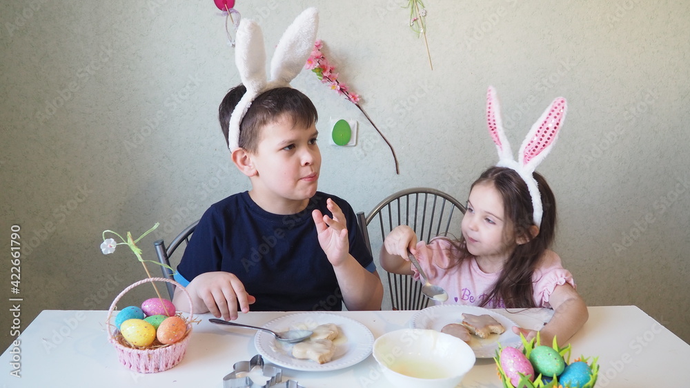 boy and girl are preparing cookies for easter, laughing. Having fun on Easter egg hunt. Child boy and girl wearing bunny ears and painting eggs. colorful eggs boy and girl are preparing cookies for easter, laughing. Having fun on Easter egg hunt. Child boy and girl wearing bunny ears and painting eggs. colorful eggs