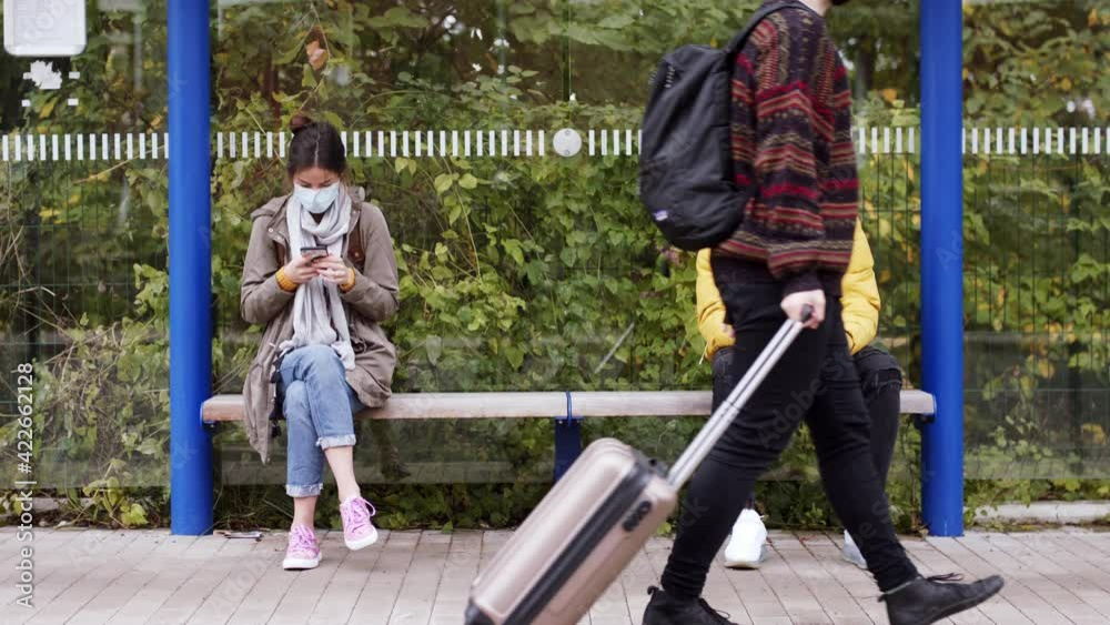 Young people with smartphone on bus stop outdoors in town. Coronavirus concept.