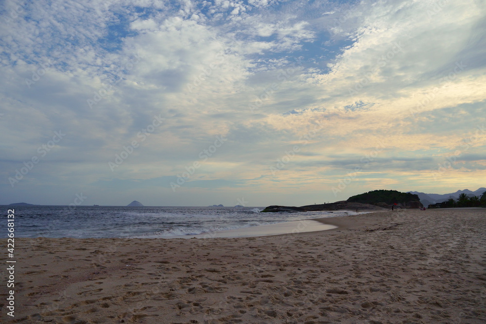 Piratininga Beach, in Niterói in Rio de Janeiro in the late afternoon. Sky with some clouds at the sunset. Sunny day and blue sky with clouds reflecting a lot of yellow and orange