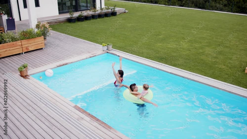 Top view of young family with small daughter in swimming pool outdoors in backyard garden, looking at camera.