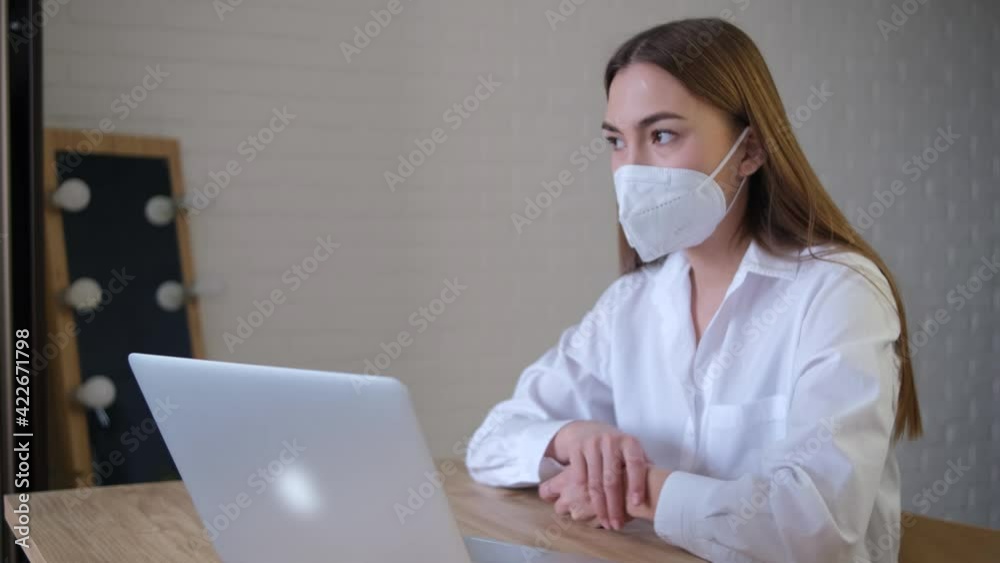 A remote employee wearing a medical mask holds a conference call with a colleague in a virtual online chat using an application launched from the home office. Classic office wear. A remote employee wearing a medical mask holds a conference call with a colleague in a virtual online chat using an application launched from the home office. Classic office wear.