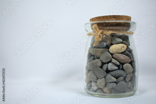 Glass jar filled with stones closed with cork and string on white background
