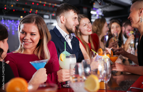 Portrait of happy young woman with colleagues enjoying corporate party in bar