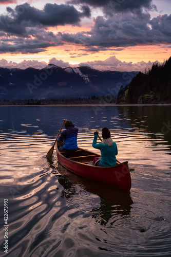 Couple friends canoeing on a wooden canoe during a colorful sunny sunset. Cloudy Sky Artistic Render. Taken in Harrison River  East of Vancouver  British Columbia  Canada.