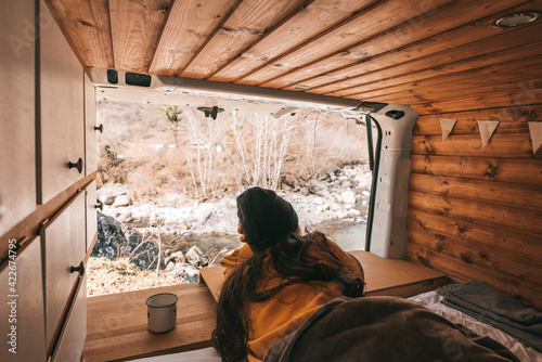 Vanlife - Young woman lying in camping van and looking at beautiful nature © RoMiEg
