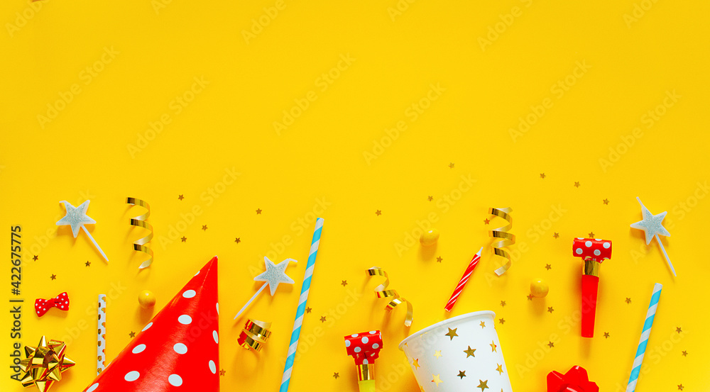 Happy birthday background: party hat, serpentine, stars, cocktail tubes, candles, blower on a yellow background.