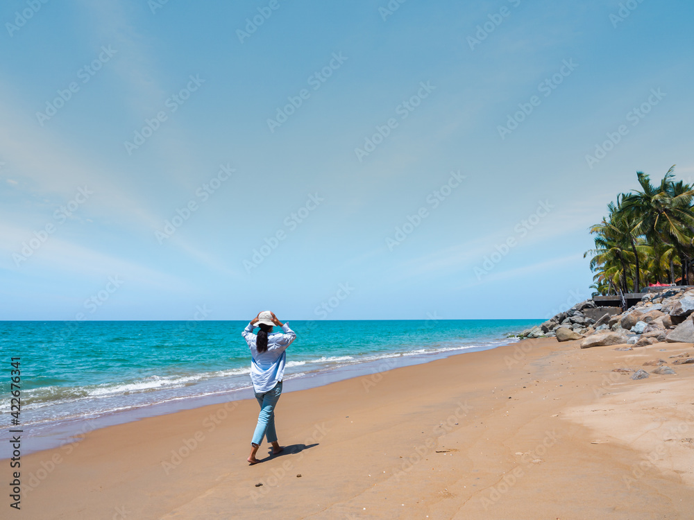 a tourist working bare foot along the sandy beach in blue wide sky and beautiful sea. open sky in summer season.  clouds sprayed over the sky. soft blue sky, blue natural background.
