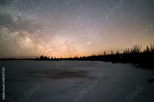 An amazing view of the Milky Way above frozen lake and forest. An awe night sky view with our galaxy.  An idyllic and motivational scenery.