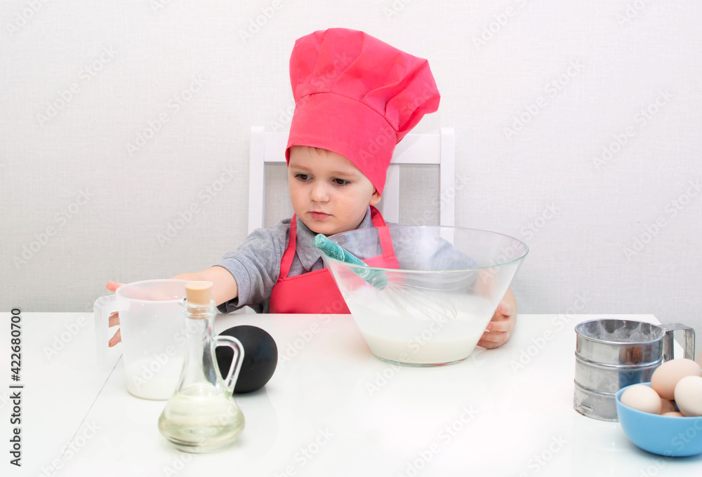 Cute little boy in a red chef hat kneads the pastry dough in a bowl. Homemade cakes Cute little boy in a red chef hat kneads the pastry dough in a bowl. Homemade cakes