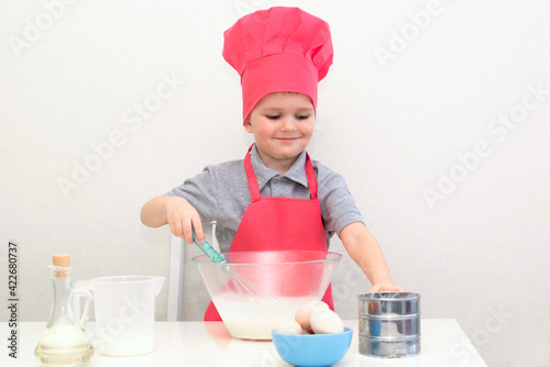 Cute little boy in a red chef hat kneads the pastry dough in a bowl. Homemade cakes