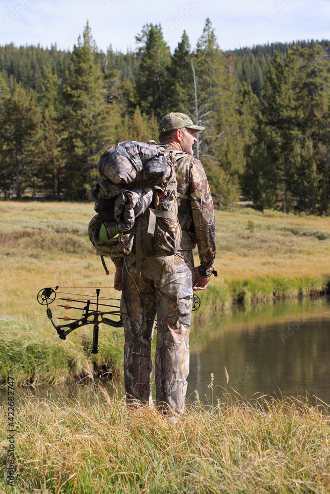 modern bow hunter in woods wearing camouflage and standing by a river