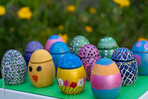 Hand-made Easter eggs on a green pedastal in front of yellow and orange spring flowers photo