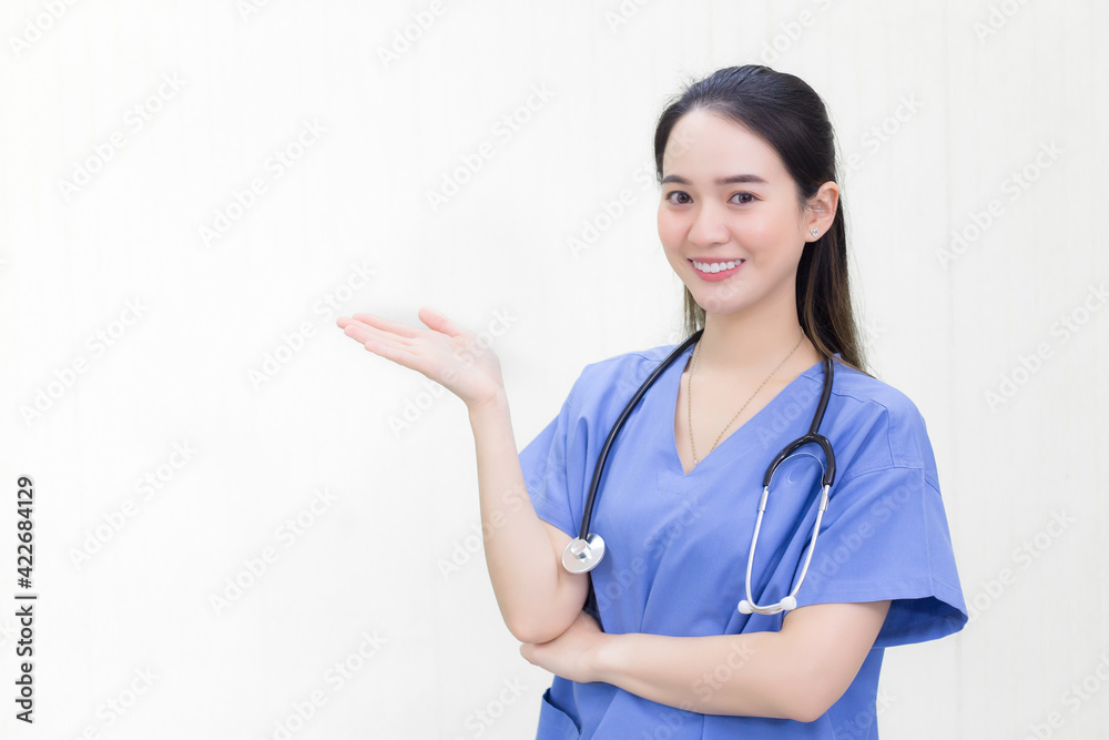 A beautiful young Asian woman doctor in a blue uniform stands and smiles while pointing to the top on a white background. A beautiful young Asian woman doctor in a blue uniform stands and smiles while pointing to the top on a white background.