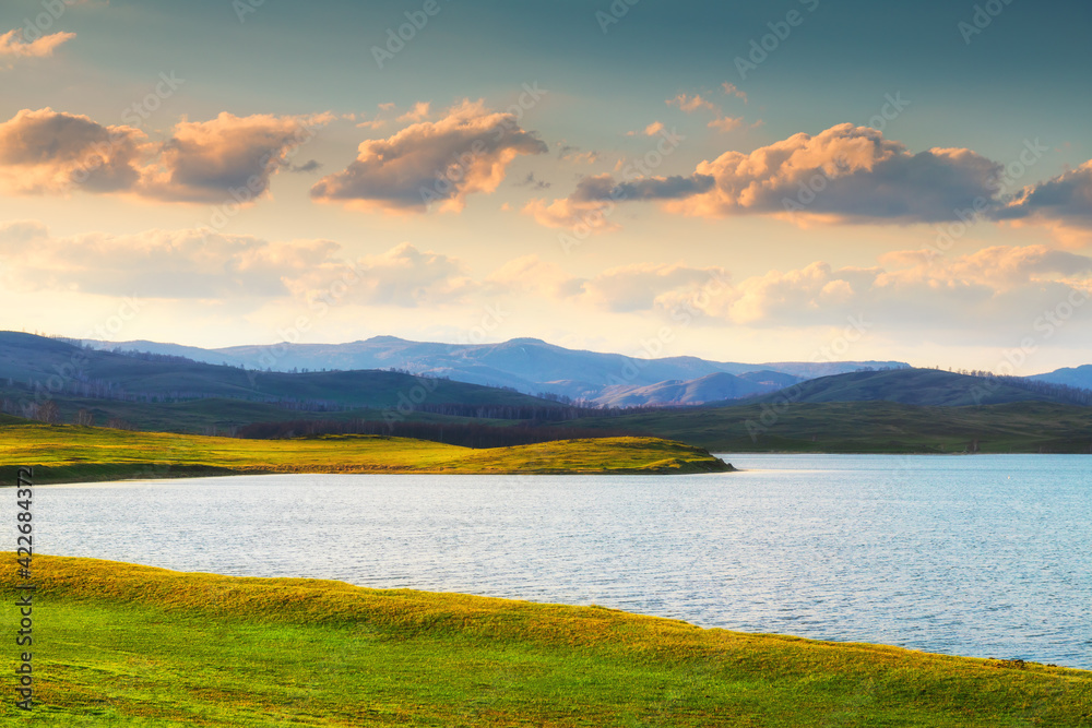 Beautiful lake in the mountains at sunset. Fresh green grass on the hill in early spring. Beautiful landscape in South Ural, Russia.