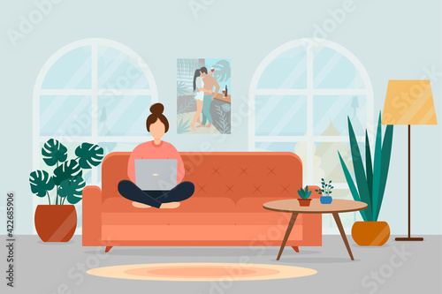 A girl with a laptop sits on a sofa in a cozy living room. Work at home and freelance concept.