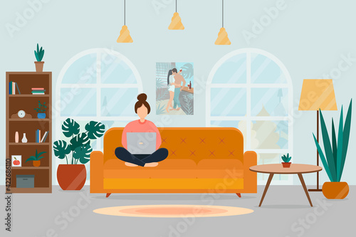 A girl with a laptop sits on a sofa in a cozy living room. Work at home and freelance concept.