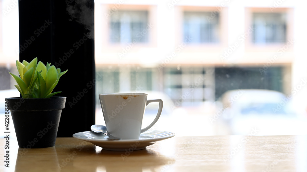 Close up view cup of hot beverage and plant on wooden table.