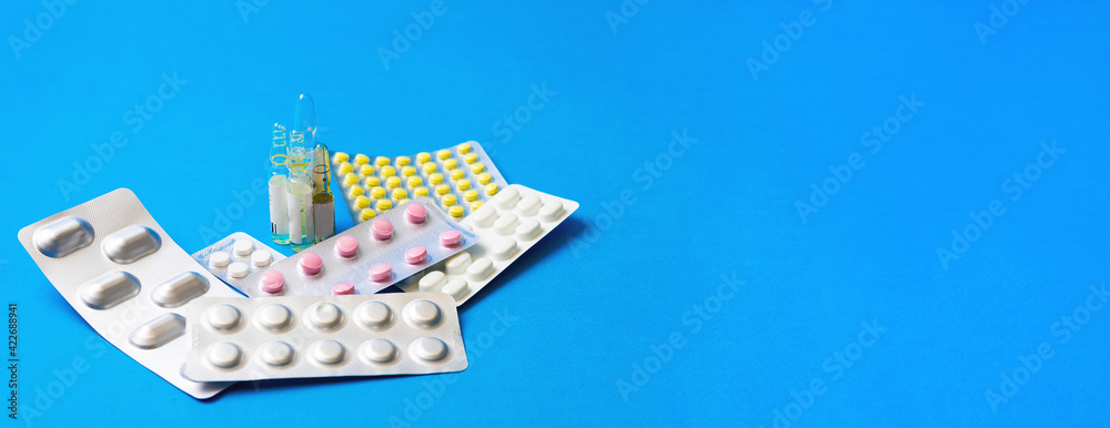 Close up medications, tablets, ampoules and syringe on blue background. Concept of treatment of influenza and viruses. Copy space