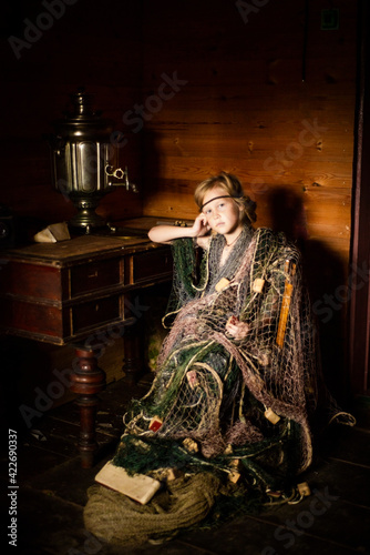 a blonde girl in a fishing net sits at a table with a samovar, a photo based on the fairy tale Seven-year-old, selective focus photo