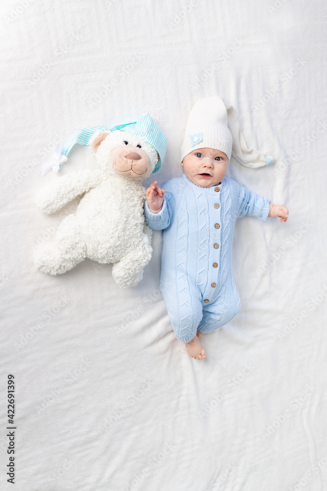 a baby on a bed in a hood goes to bed or wakes up in the morning. Textiles and bedding for children. Newborn baby with a toy bear a baby on a bed in a hood goes to bed or wakes up in the morning. Textiles and bedding for children. Newborn baby with a toy bear
