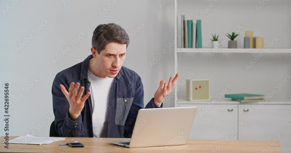 Caucasian man millennial user sitting at table looking at laptop computer screen feeling angry rage, screaming in irritation worried about error in online service or bad news, receives rejected email