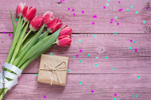 A bouquet of tulips and a gift box on a pink wooden background. Floral background in with sequins.