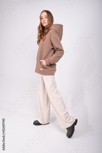 Full length isolated portrait of young woman wearing stylish outfit with set of tracksuit,hoodie and beige trousers. Pretty woman layered outfit. Oversize clothes.