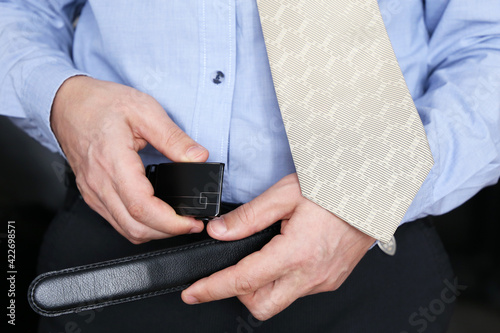 Man in office clothes unbuttons his pants belt, sex at work concept