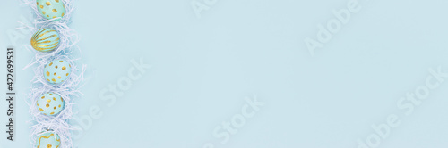 Fashion easter banner - blue eggs with golden design in white nest as border on blue color, top view. photo