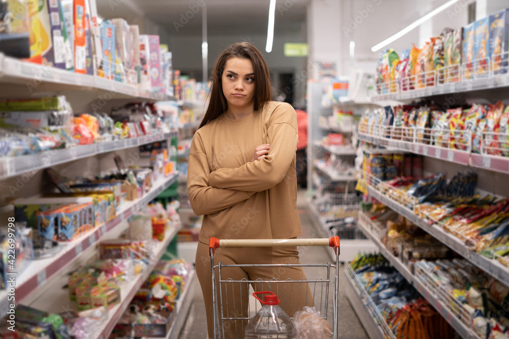 Serious woman with shopping cart at the grocery store. Attractive young woman. Long black hair.